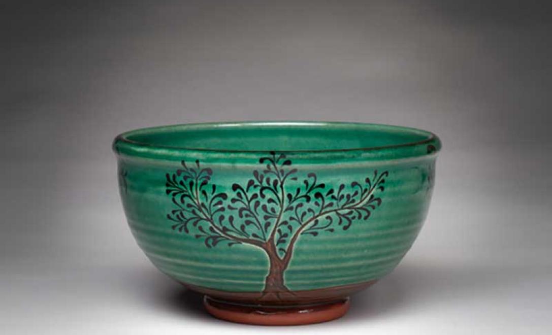 Bol de poterie fini magnifiquement vitré avec la coloration verte et l’image de deux arbres en brun.