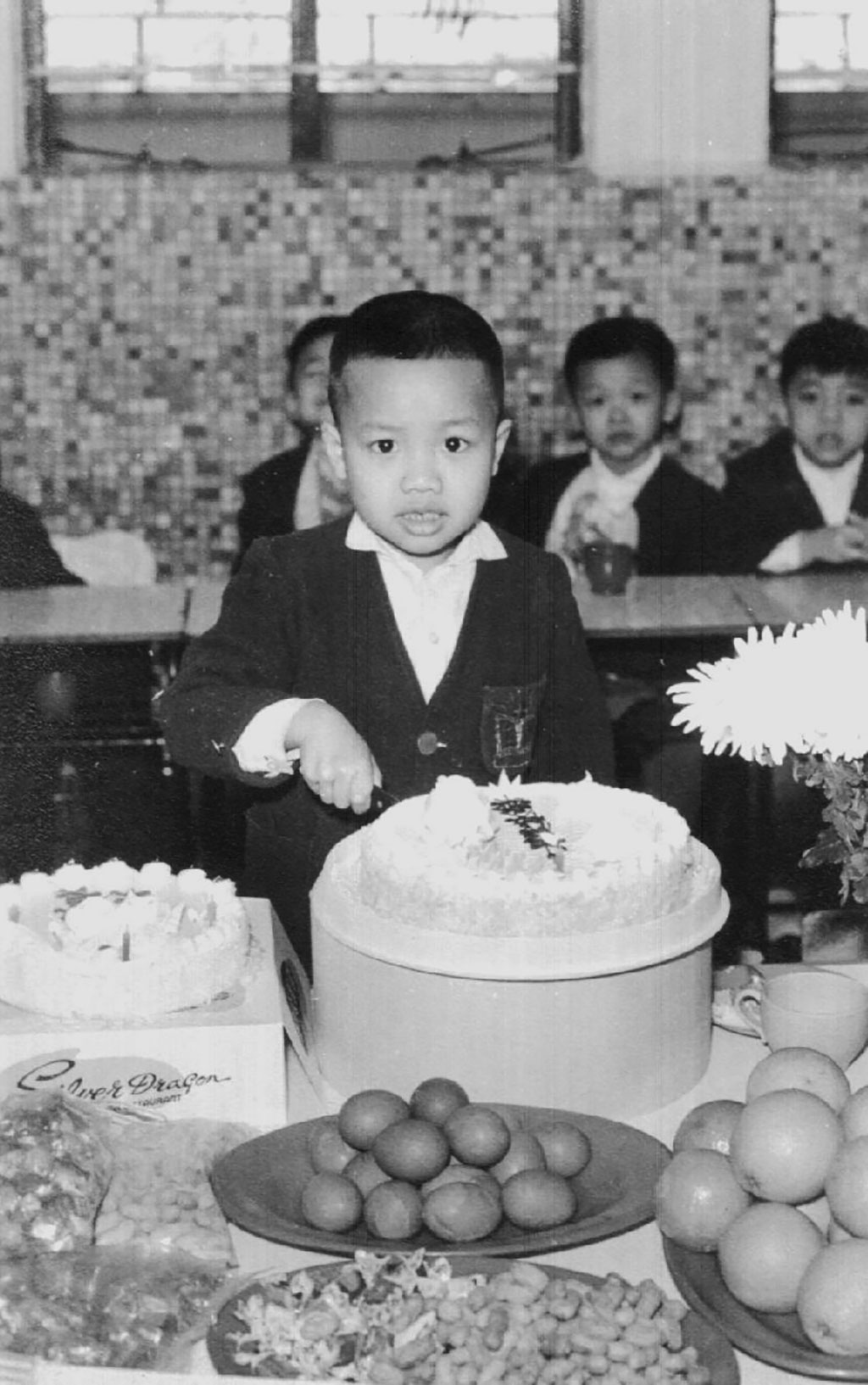 Un jeune garçon en costume regarde la caméra alors qu’il coupe un gros gâteau d’anniversaire.