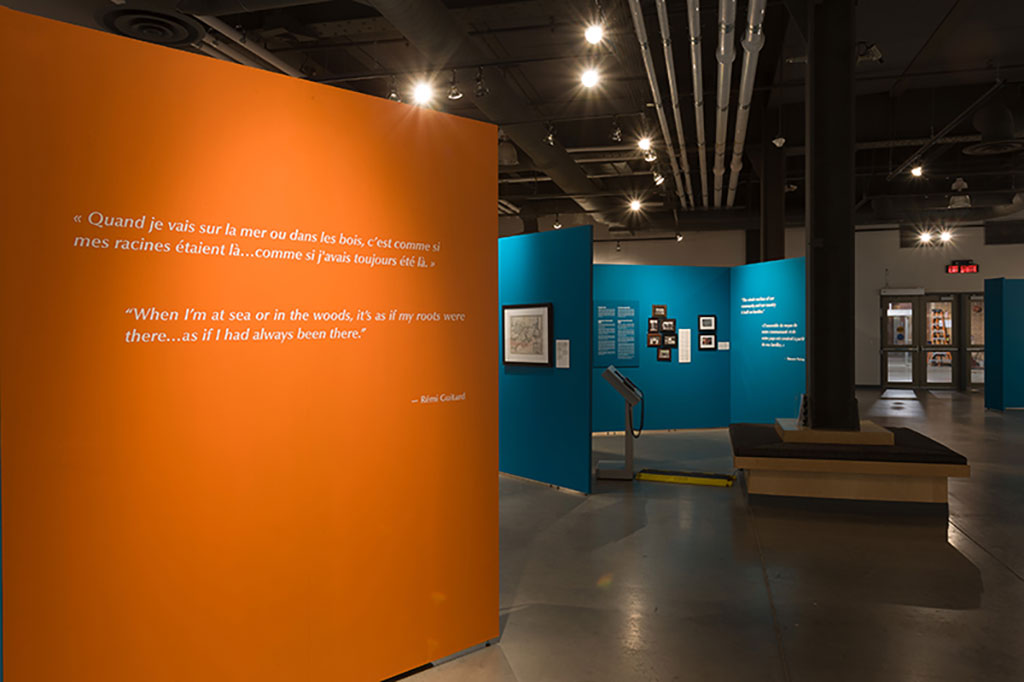 Une salle d’exposition avec de grands panneaux orange et turquoise où sont affichés des images et du texte.