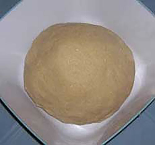 Une masse ronde d'une matière ressemblant à du pain, placée dans une assiette carrée de couleur blanche.