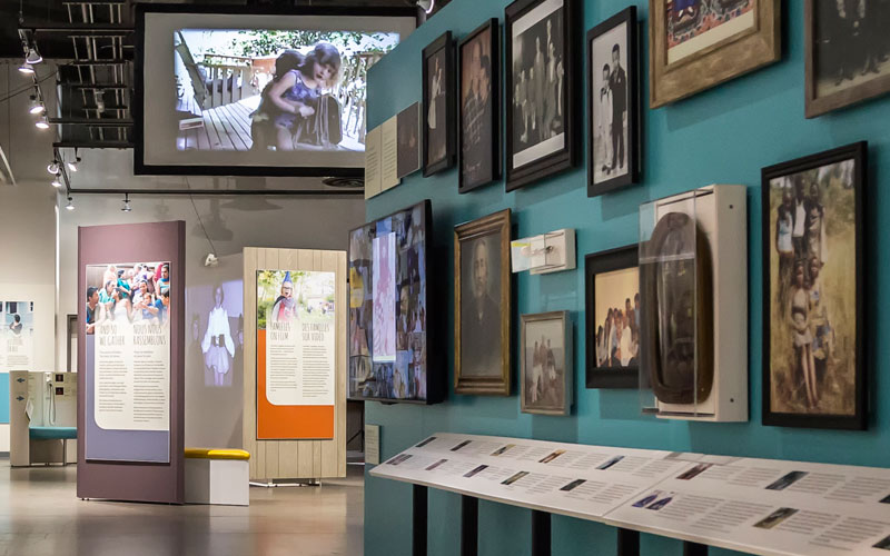 Une image de l’exposition présentant des photos de famille encadrées sur le mur et des panneaux d’exposition.