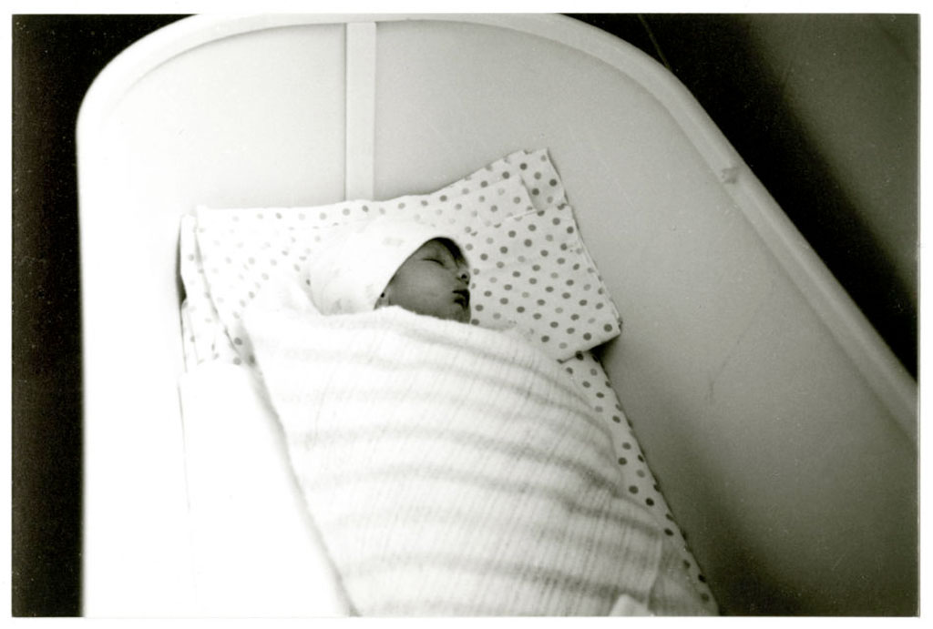 Un bébé emmailloté dans une couverture dort dans un lit d’enfant blanc.