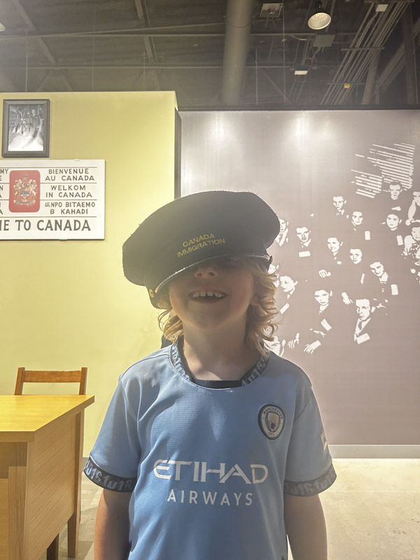 Un garçon de 9 ans sourit, coiffé d’une casquette d’agent de l’immigration canadienne trop grande pour lui.