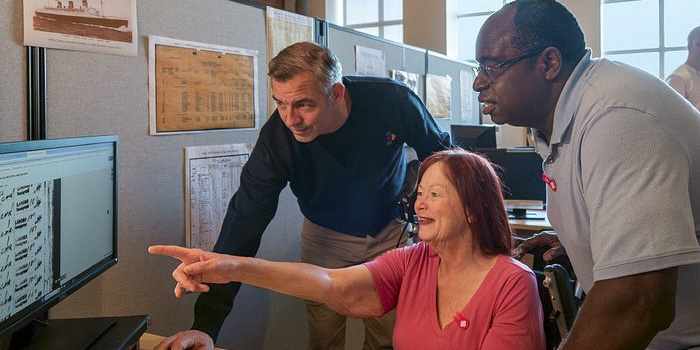 Un membre du personnel du Musée montre quelque chose sur un écran d’ordinateur à des visiteurs ravis.