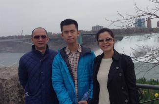 Un jeune homme se tient entre ses parents avec Niagara Falls en arrière-plan.