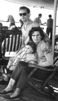 Femme assise sur chaise longue, un bébé sur ses genoux et un homme sur l’accoudoir