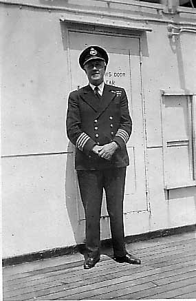 Un homme se tient devant la porte d’un navire et porte un uniforme de capitaine.