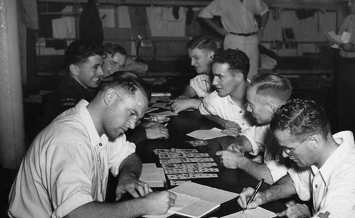 Groupe de jeunes hommes assis autour d’une table jouant aux cartes et écrivant sur un tableau.