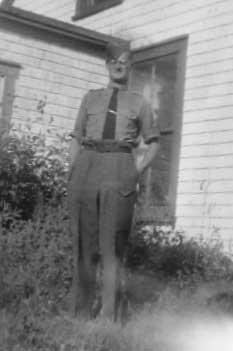 Un homme portant des vêtements militaires et des lunettes se tient devant une fenêtre.