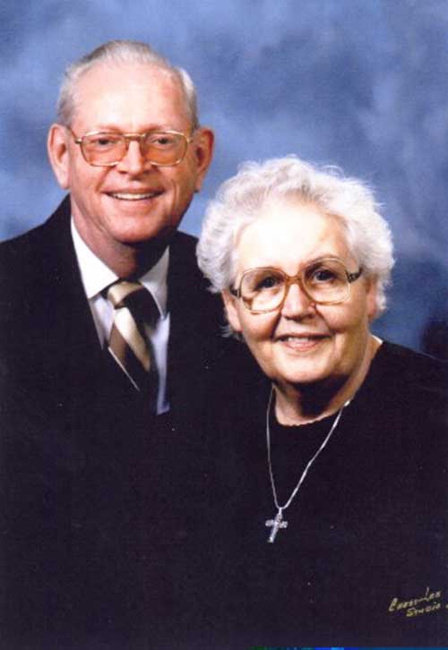 Couple âgé bien habillé portant des lunettes et posant pour une photo.