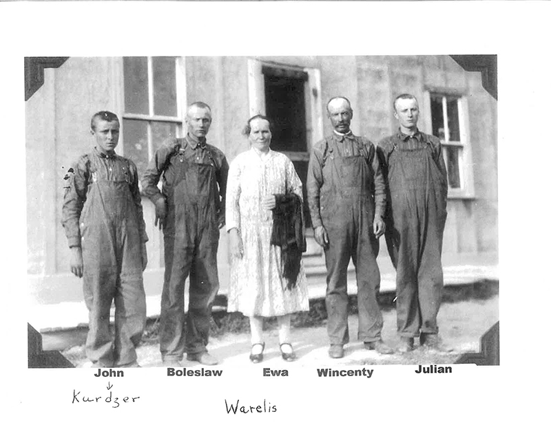 Quatre hommes en uniforme de construction et une femme en robe blanche debout devant l’immeuble.