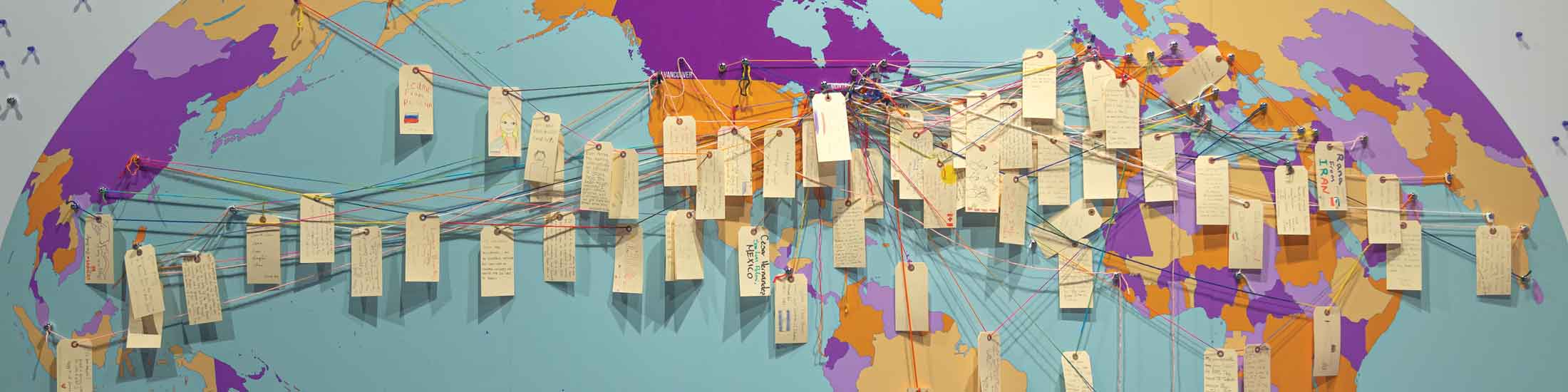 Des étiquettes de bagage avec des notes de visiteurs sont attachées avec une ficelle sur une grande carte du monde.