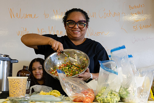 Une Caribéenne souriante brandit un bol en métal rempli de légumes coupés.