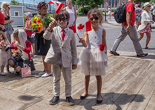 Deux enfants debout devant le Musée agitent des drapeaux canadiens.