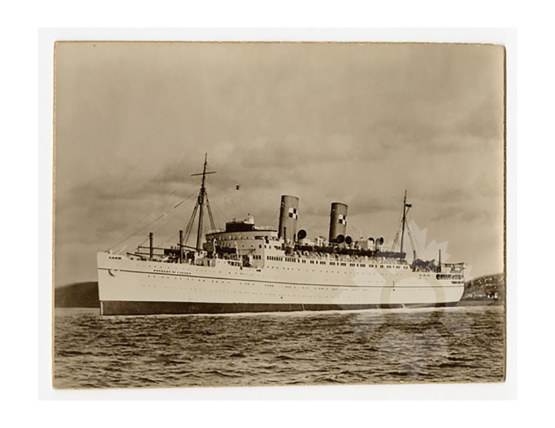 Image en noir et blanc du RMS Empress of Canada II en mer, vu de profil bâbord, avec ses deux cheminées et des collines côtières en arrière-plan.