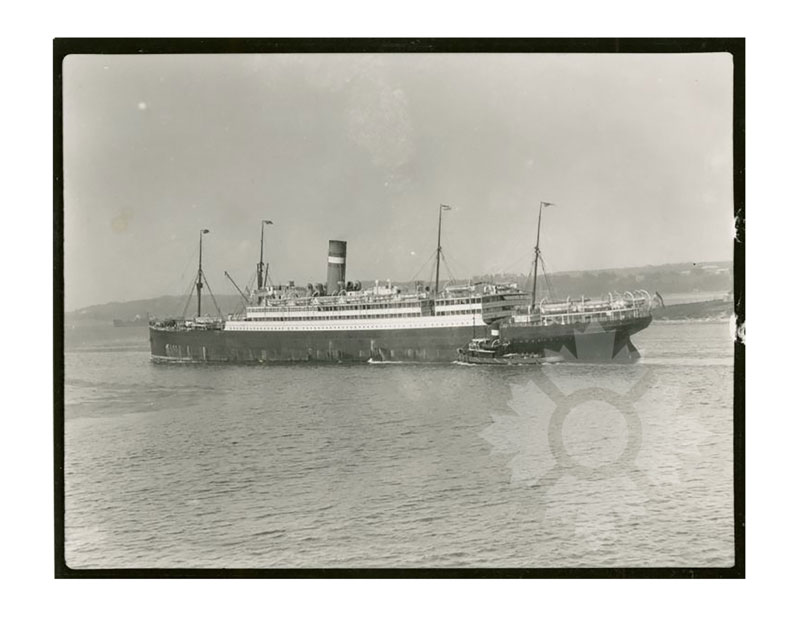 Image en noir et blanc du SS Nieuw Amsterdam I en mer, vu de profil bâbord, avec un remorqueur à ses côtés.