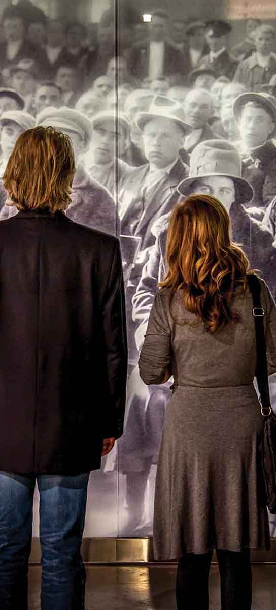 Un homme et une femme regardent une photographie historique grandeur nature d’immigrants qui attendent leur tour.