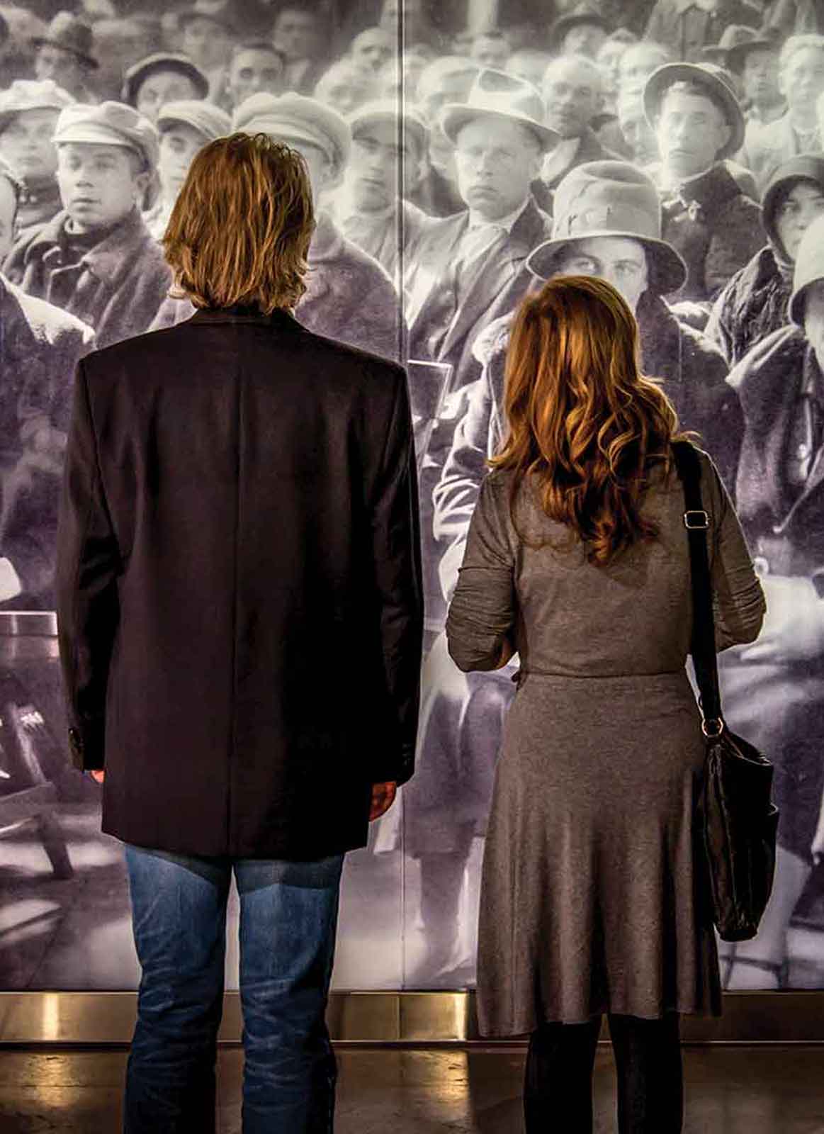 Un homme et une femme regardent une photographie historique grandeur nature d’immigrants qui attendent leur tour.