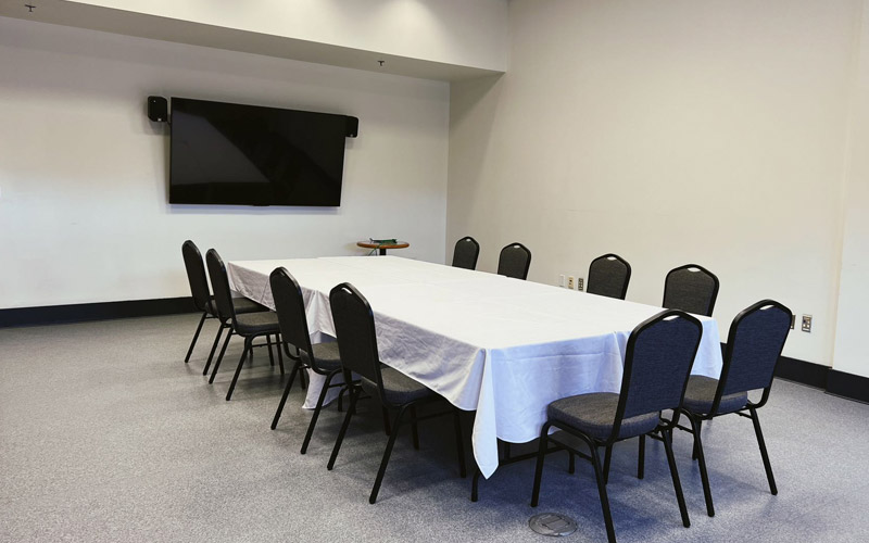 Une petite pièce aux hauts plafonds, équipée pour les présentations d’une grande table de réunion pour huit personnes et d’un téléviseur avec deux haut-parleurs.