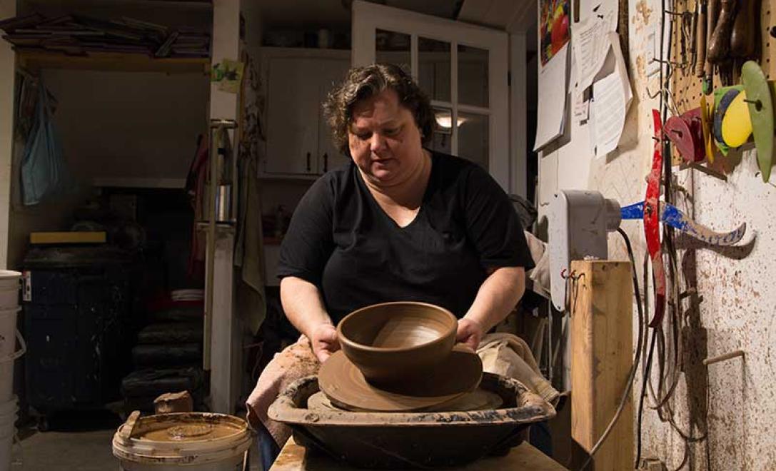 La femme en tee shirt noir présente un bol en céramique fini dans son atelier.