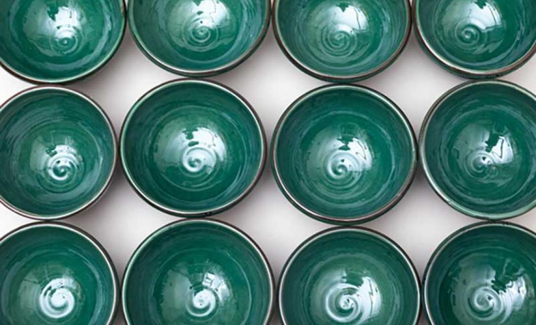 Vue aérienne de plusieurs nouveaux bols de poterie s’assoient côte à côte, tous magnifiquement vitrés en vert.