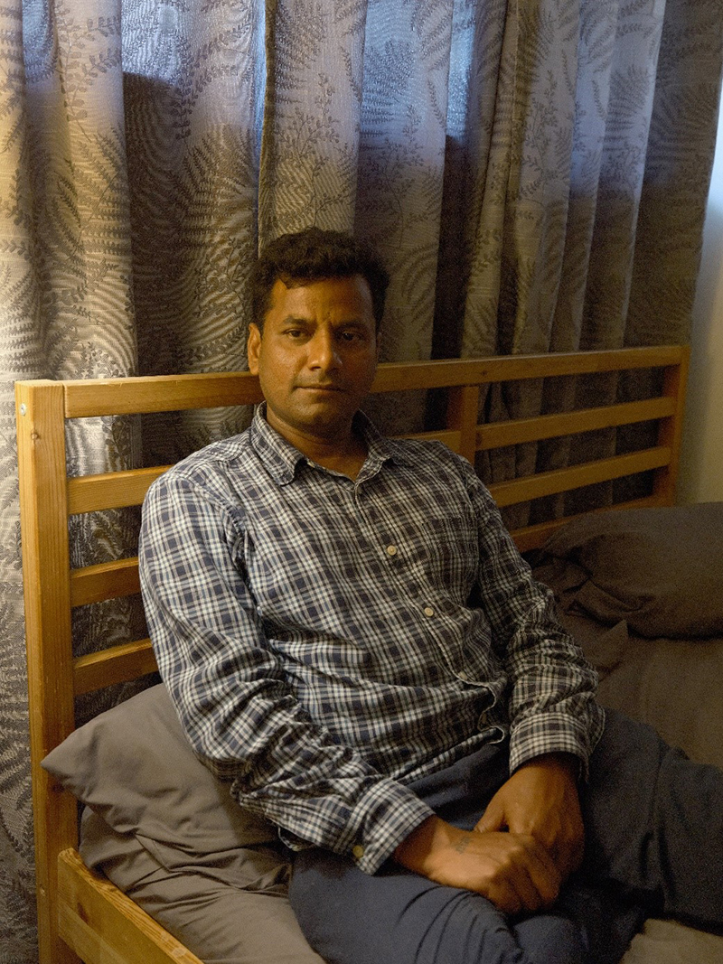 Un homme est assis sur un lit en bois avec des rideaux derrière lui.