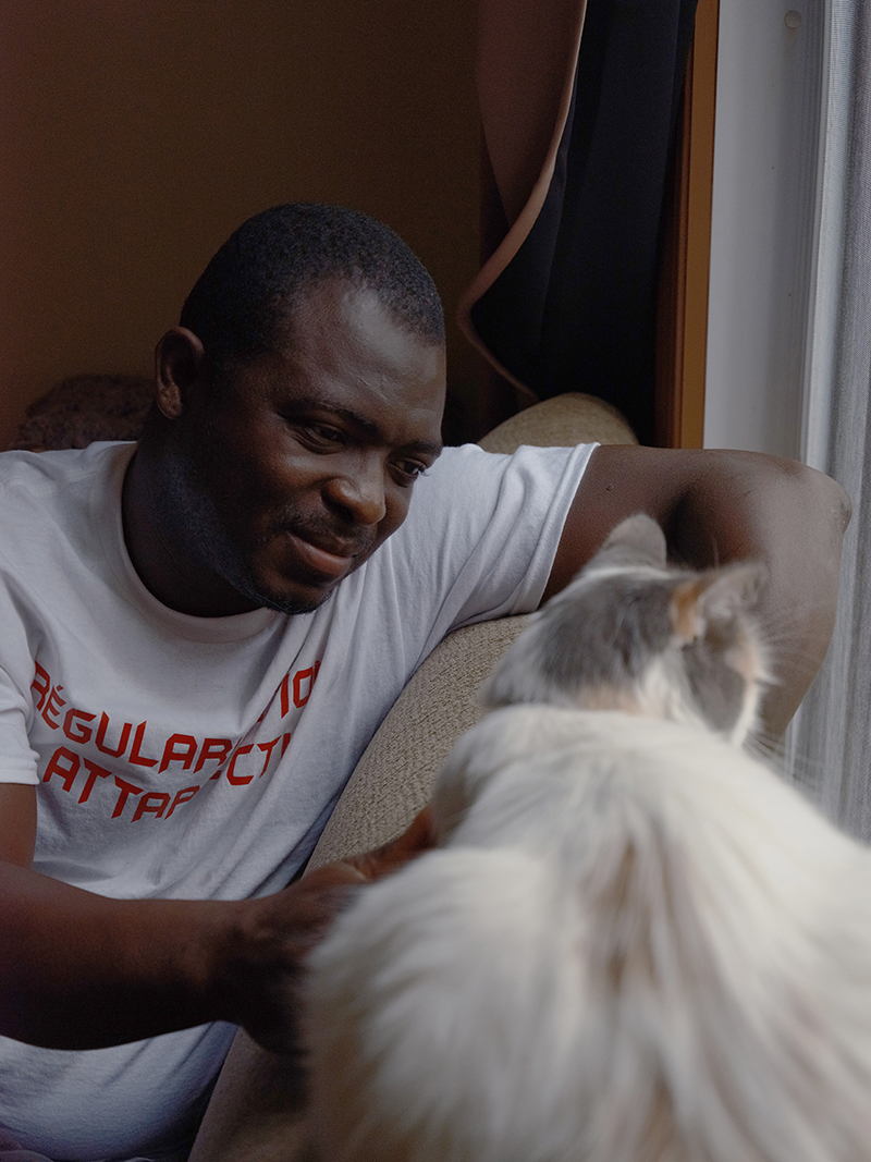 Un homme en chemise blanche s’assoit et joue avec un chat poilu.
