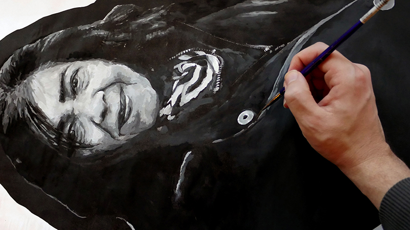 Main d’artiste faisant des coups de pinceau sur une peinture d’une femme.