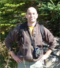 Un homme, vêtu d'une chemise et d'un pantalon kaki et portant un sac à dos, se tient sur un terrain rocheux.