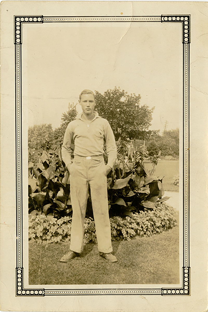 Un jeune homme avec les mains dans les poches se tient devant un jardin.