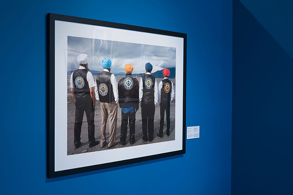 Cinq hommes portant des turbans et des manteaux de cuir tournent le dos à la caméra et regardent l’horizon.