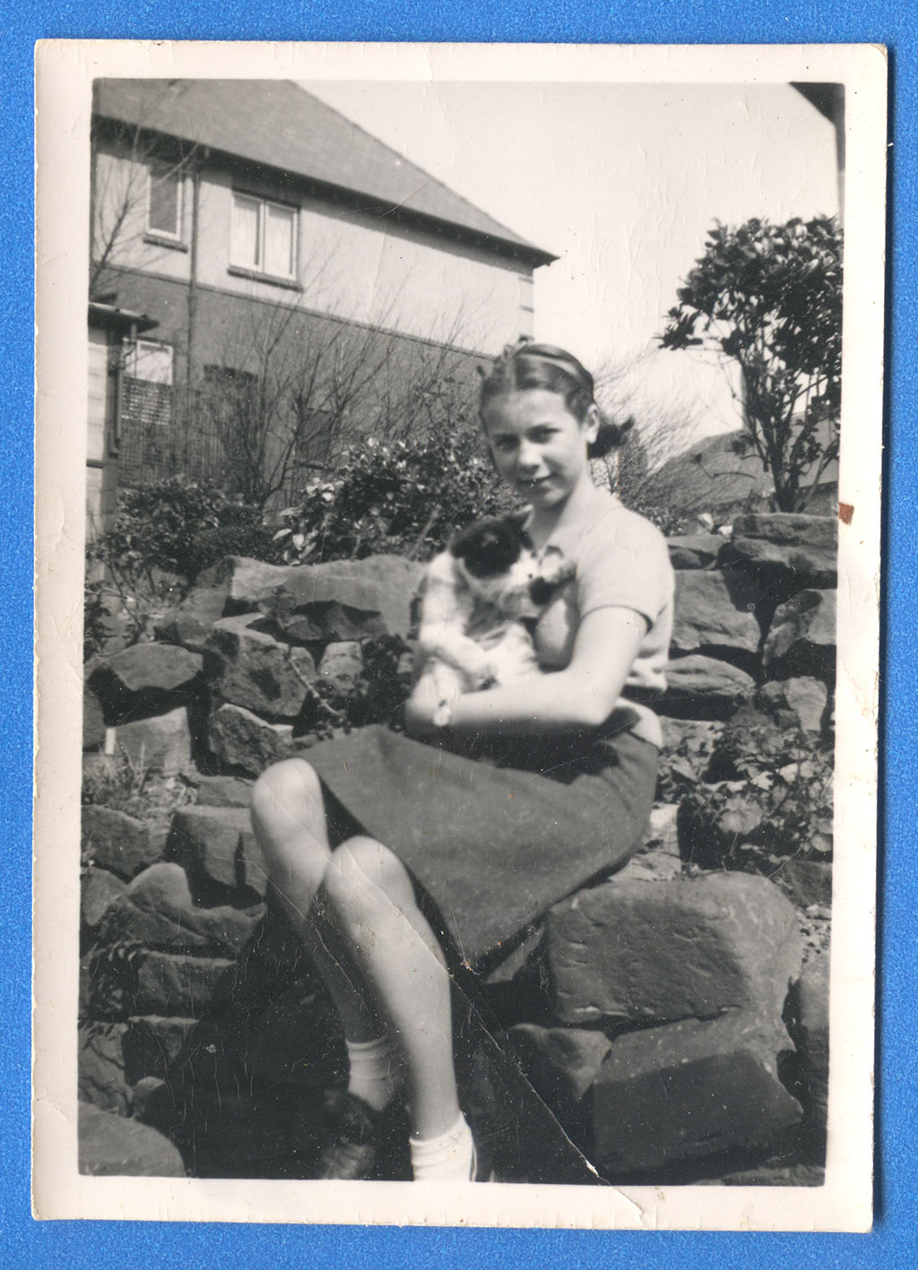 Une jeune femme assise sur un mur de pierre. Elle tient un chat dans ses bras.