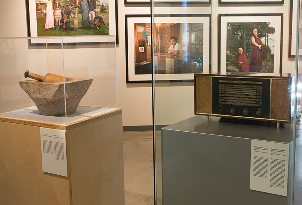 Une salle d'exposition dans laquelle se trouvent deux artéfacts contenus dans des vitrines et des portraits encadrés en arrière-plan.