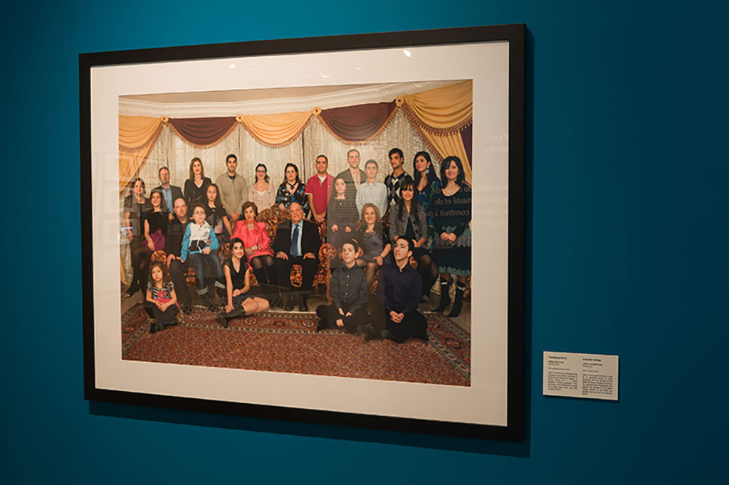 Un magnifique portrait coloré montrant une grande famille. La photo est installée sur un mur de couleur sarcelle.