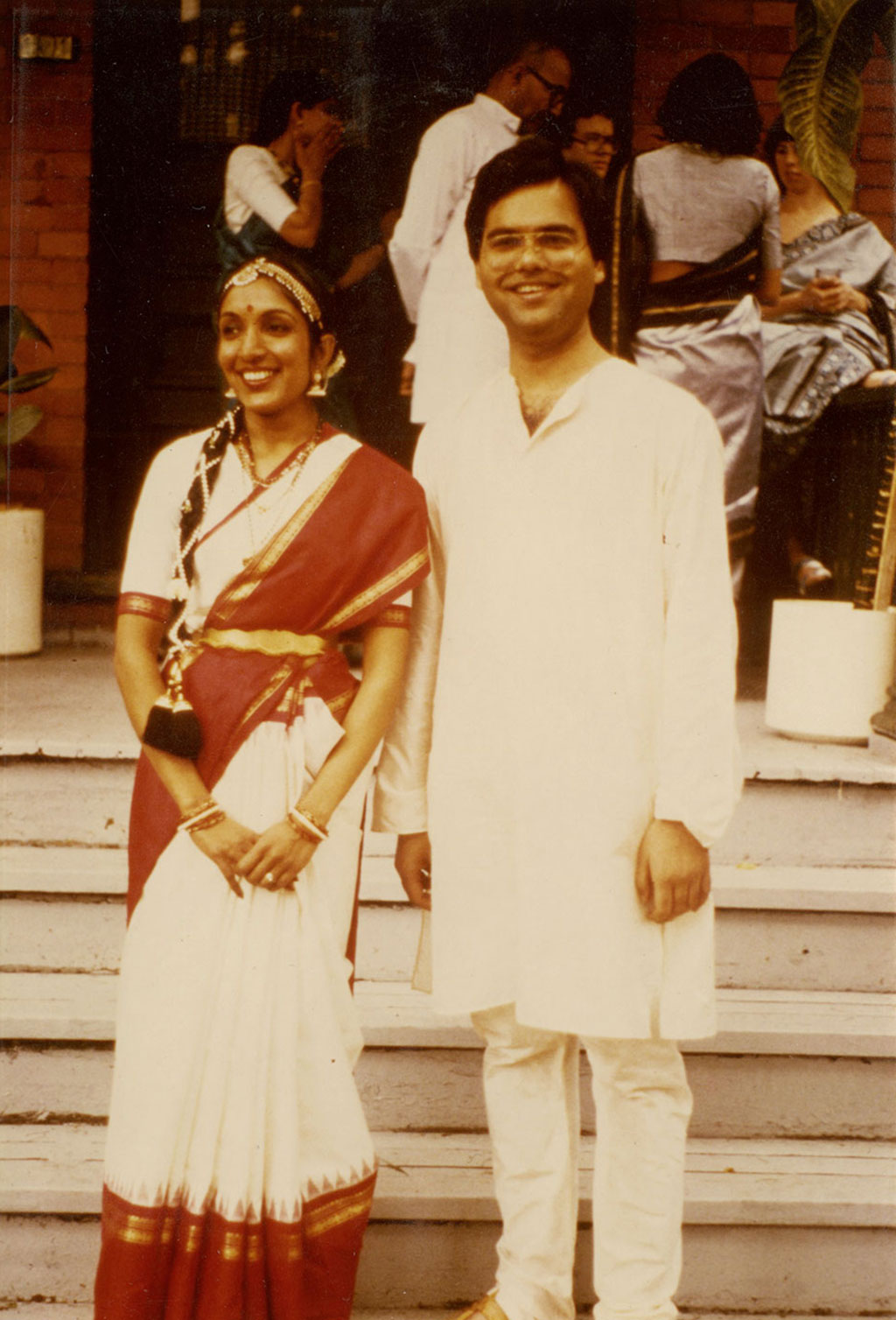 Un jeune couple en costume indien traditionnel se tient debout, souriant.