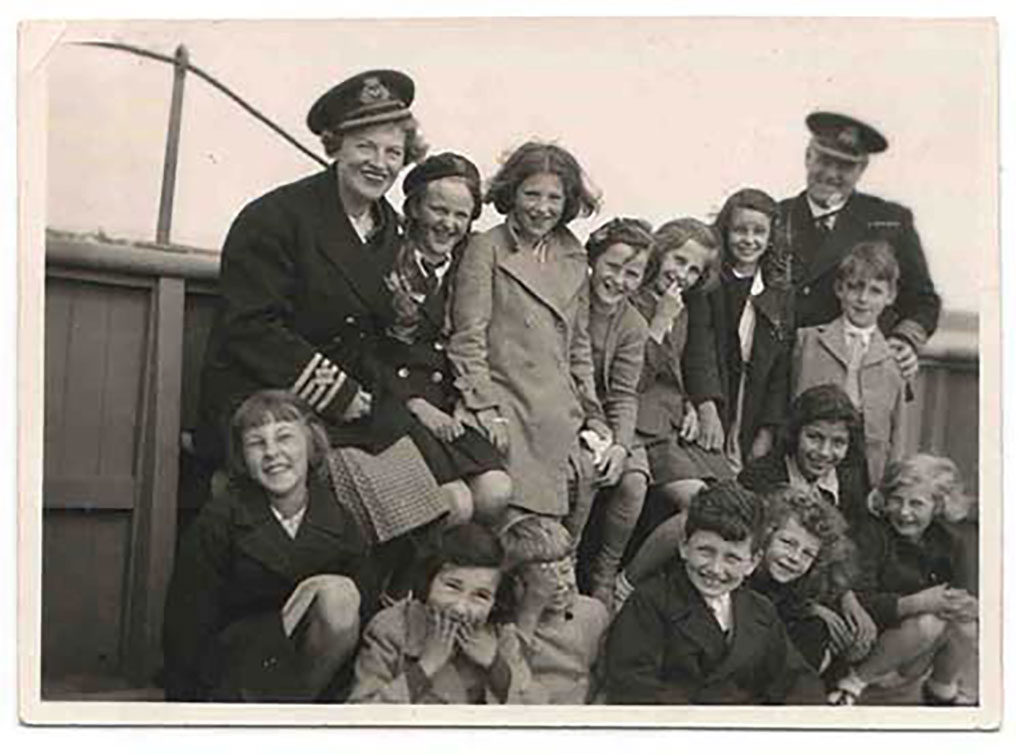 Une femme en uniforme de capitaine entourée d'enfants de différents âges. Certains enfants sont assis et certains sont debout.