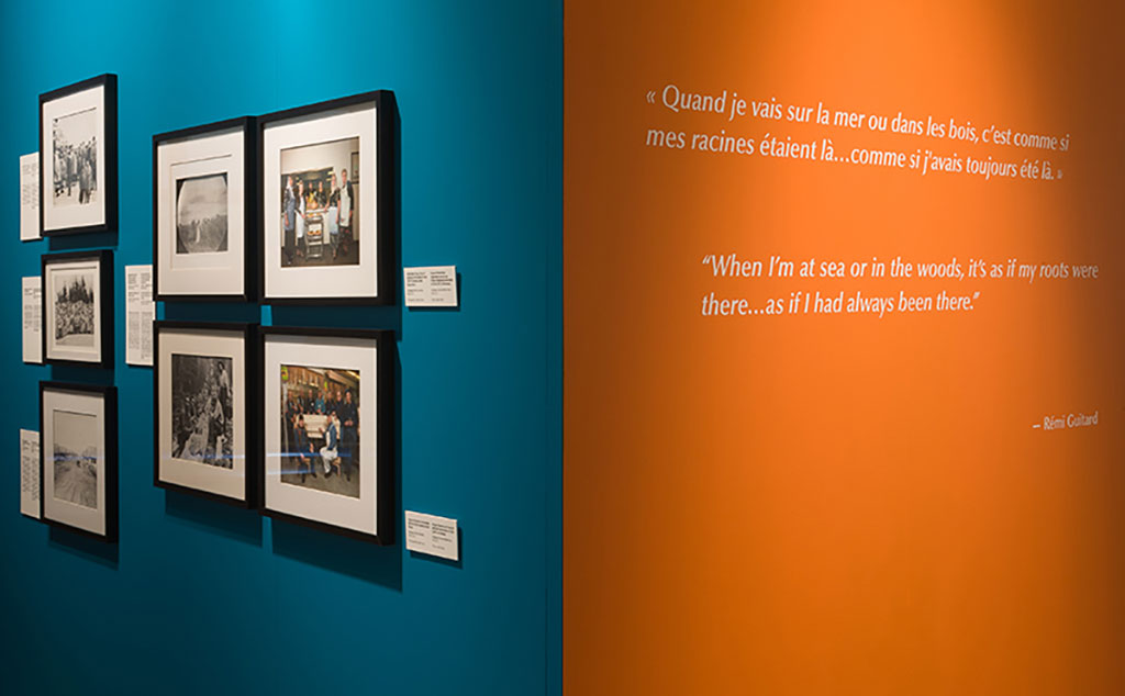 Une salle d’exposition avec de grands panneaux orange et turquoise où sont affichés des images et du texte.