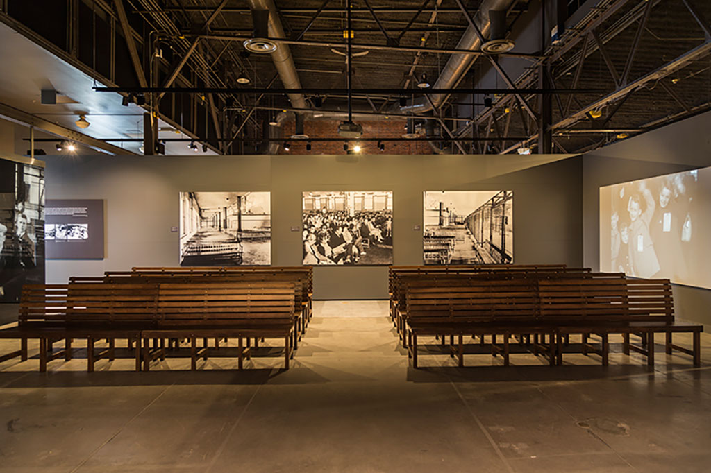 Des rangées et des rangées de bancs font face à un mur avec des images projetées en noir et blanc.