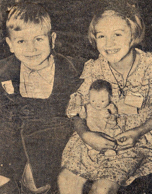 Un jeune garçon et une jeune fille sont assis ensemble et sourient. La jeune fille tient une poupée.