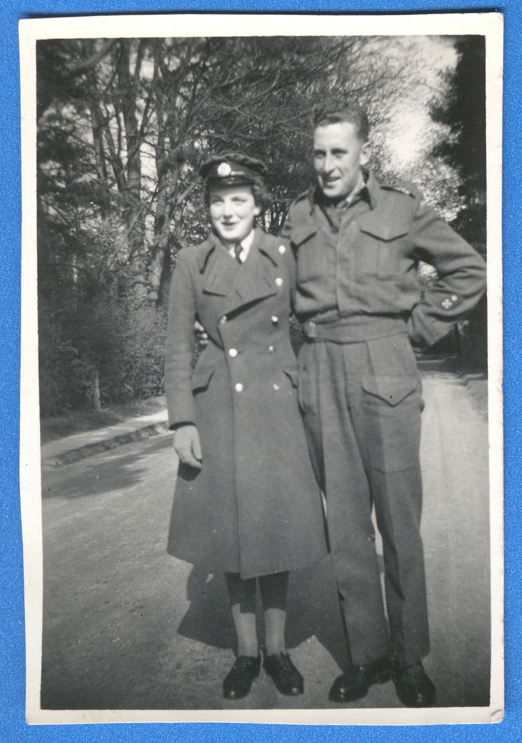 Un homme et une femme en uniformes militaires, bras dessus, bras dessous, sur une route de terre.