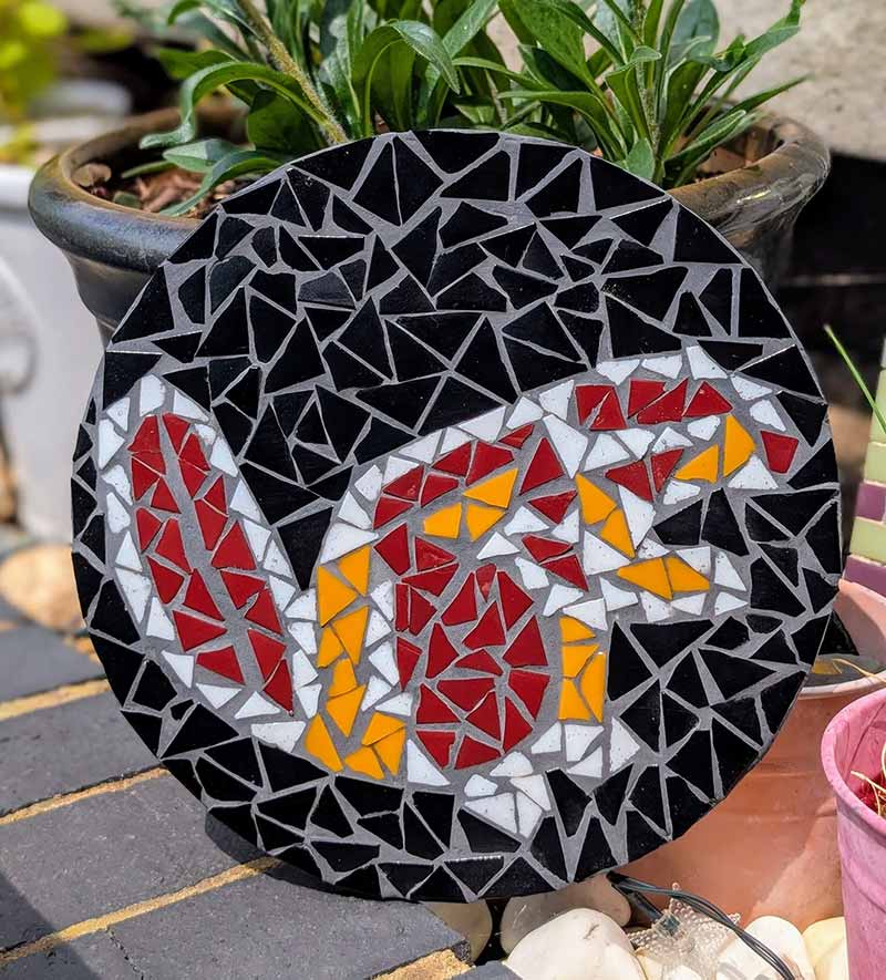 Panneau de mosaïque circulaire représentant un castor en carreaux de verre rouge, blanc et orange sur fond noir.