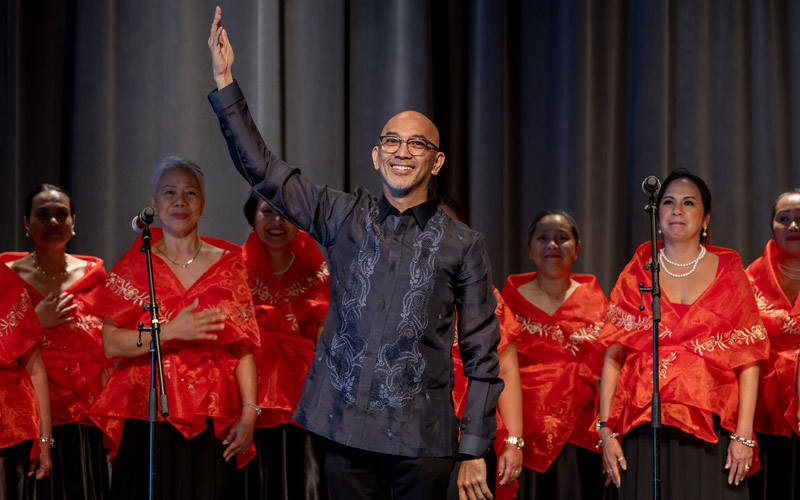 Un groupe de femmes philippines en vêtements rouges sourient derrière un homme philippin chauve.