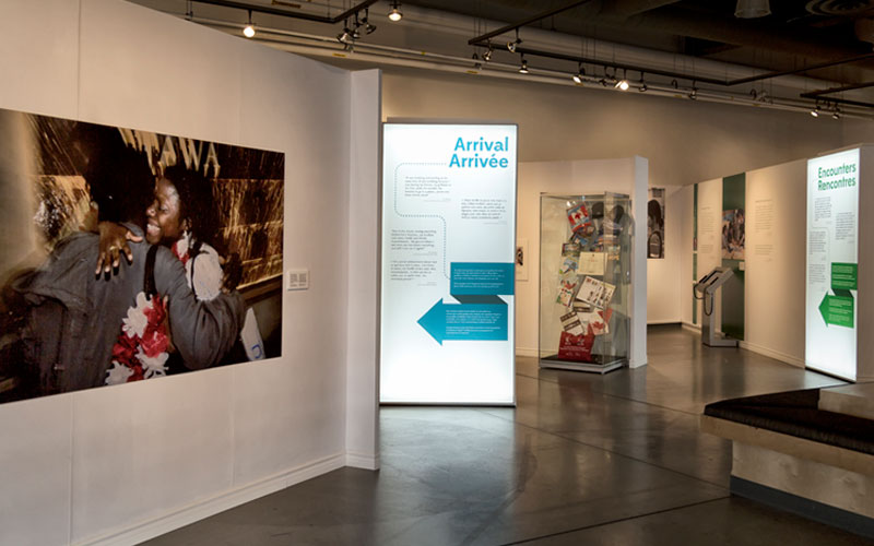 Une image de l’exposition, dont une photographie de deux personnes s’étreignant, des panneaux de texte et une vitrine en verre contenant des objets.