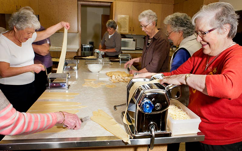 Sept femmes préparent des pâtes dans une cuisine.