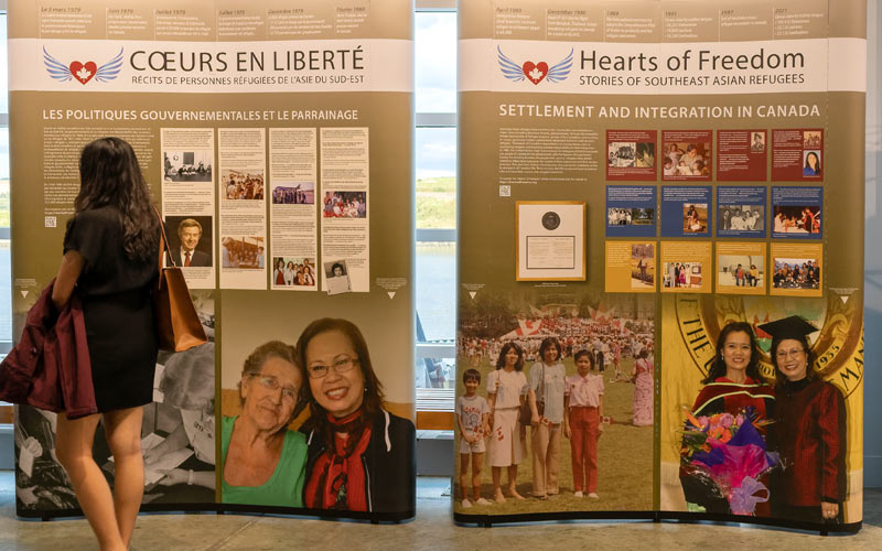Une femme passe devant deux panneaux d’exposition présentés en anglais et en français.