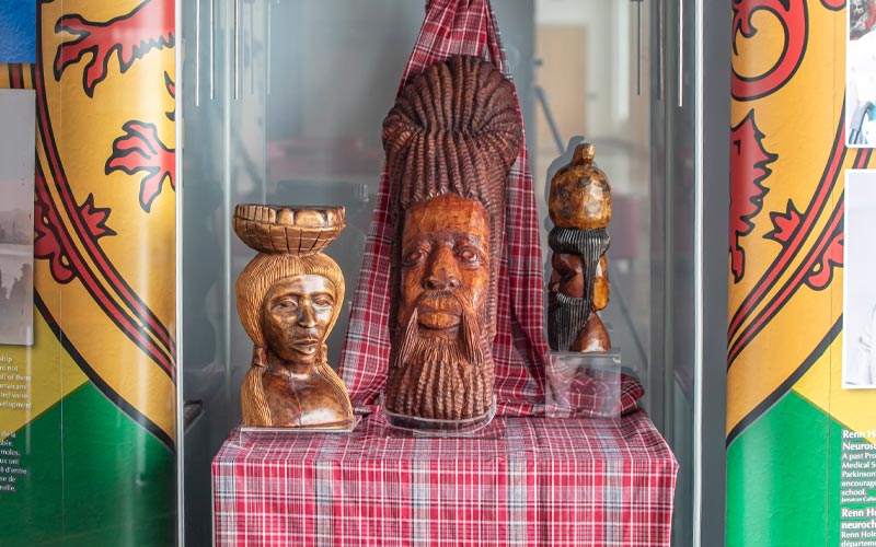 Trois objets en bois de la Jamaïque sont exposés dans une vitrine en verre.