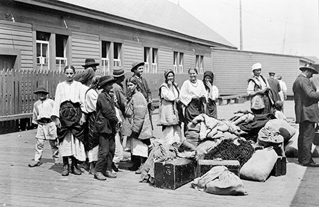 Vieille photo en noir et blanc sur laquelle se trouvent des immigrantes ukrainiennes magnifiquement vêtues. Elles ont des sacs de voyage et attendent quelque chose.