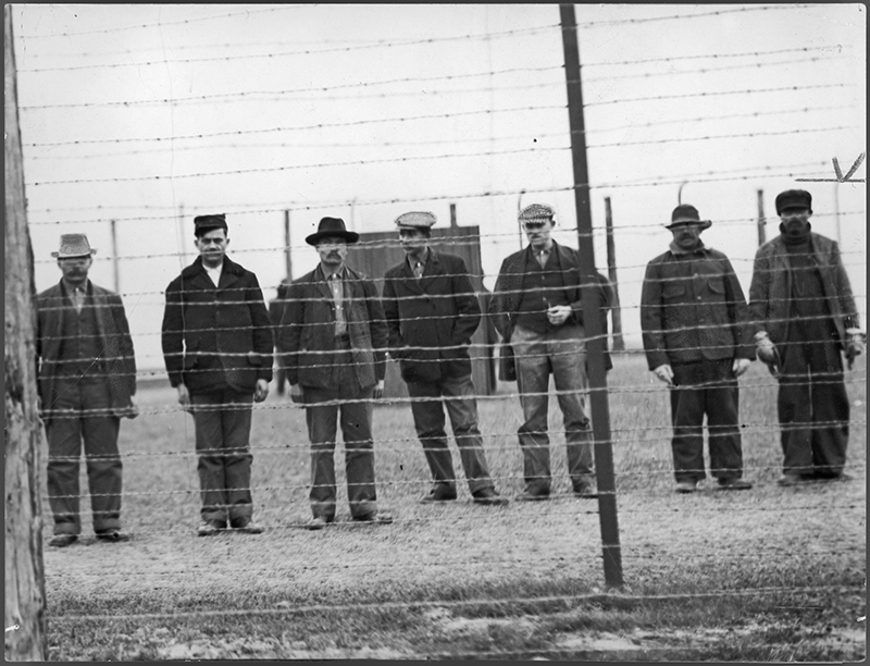 Image d’archives de plusieurs hommes debout derrière une clôture de barbelés.