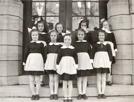 Neuf jeunes filles en uniforme sur les marches d'un bâtiment en pierre.