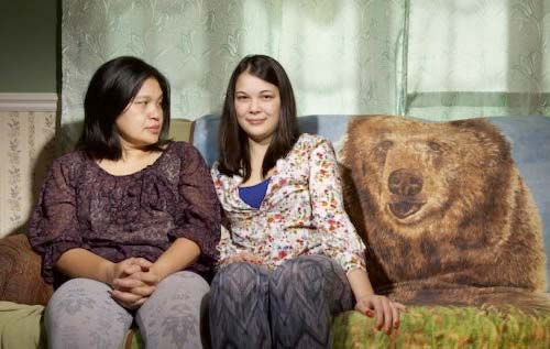 Deux femmes assises sur un canapé. Au dos du canapé se trouve une grande couverture avec un gros visage d'ours.